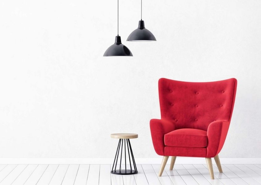 Modern wing back chair in bright red in empty room with white walls and black hanging pendant lights