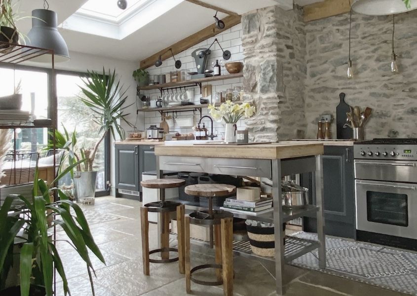 Rustic open plan kitchen with stone wall and wooden breakfast bar with industrial stools