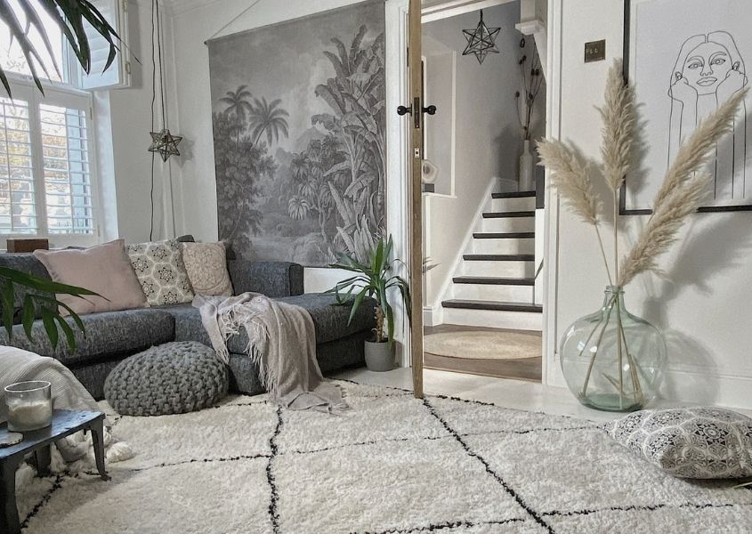 Living room with large cream rug, grey sofa, large glass floor vase with pampas grass and a grey mural on the wall