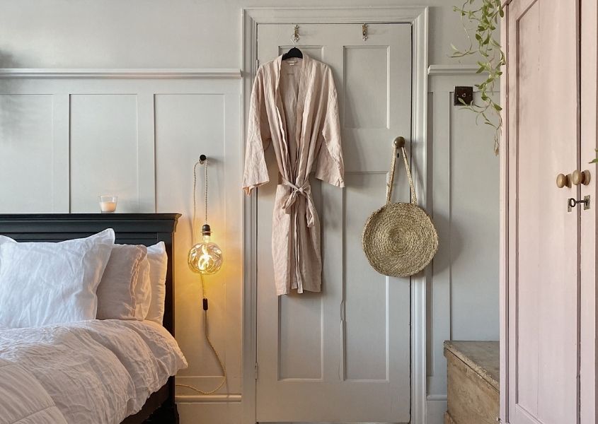 Back of white painted bedroom door with pale pink dressing gown hanging on it, with wood paneled wall and wooden bed