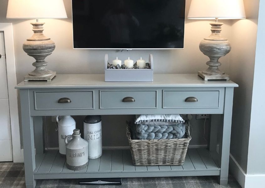 Grey painted wooden console table with three drawers and three draws with tv on top