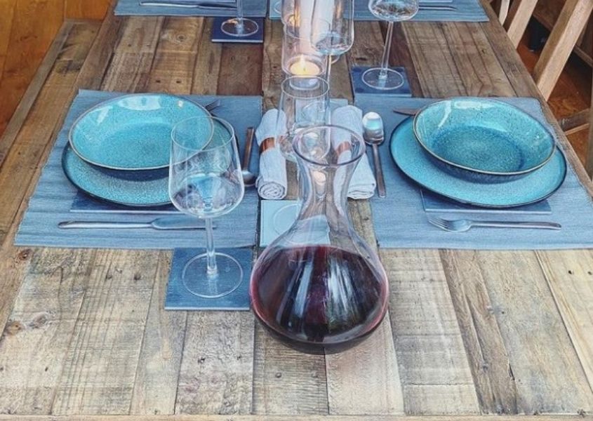 Reclaimed wood dining table with carafe of red wine, blue plates and placemats set for two
