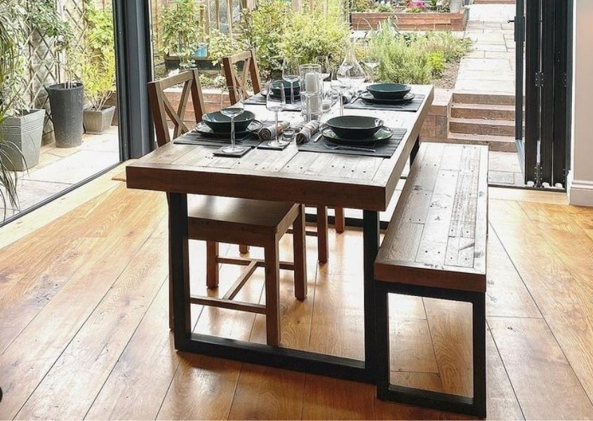 Industrial dining table with black metal legs and matching wooden bench in dining room with open bi-fold doors