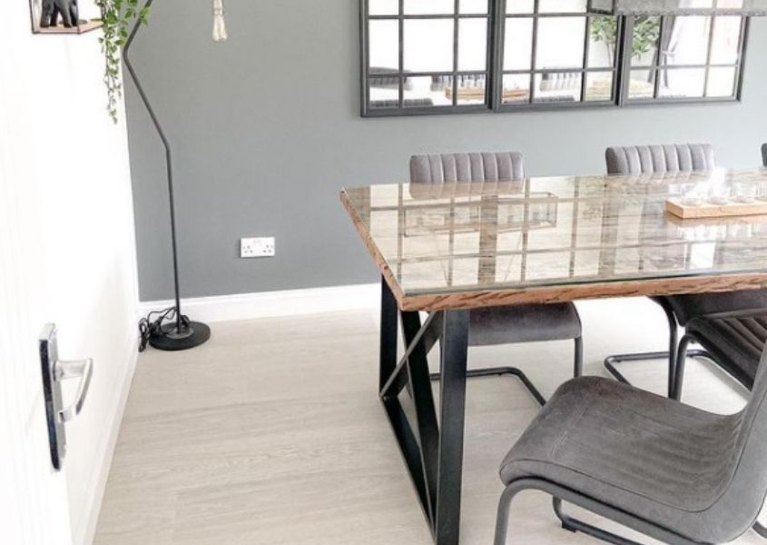 Industrial dining table with black criss-cross legs and glass top, with grey faux leather dining chairs