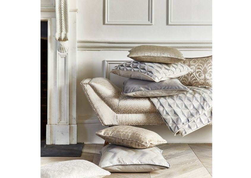 Pile of fabric cushions in silver, white and grey on a fabric chaise long