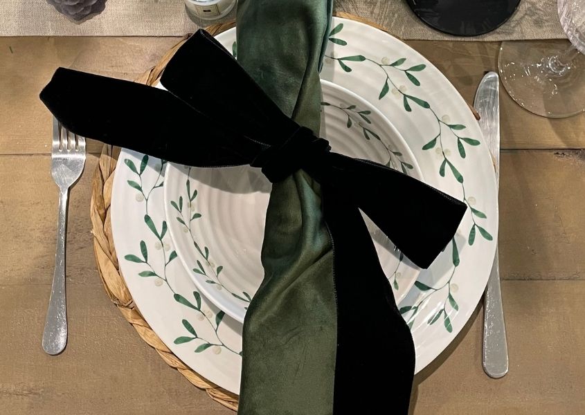 white Christmas plate with green velvet napkin and black velvet bow on reclaimed wood dining table