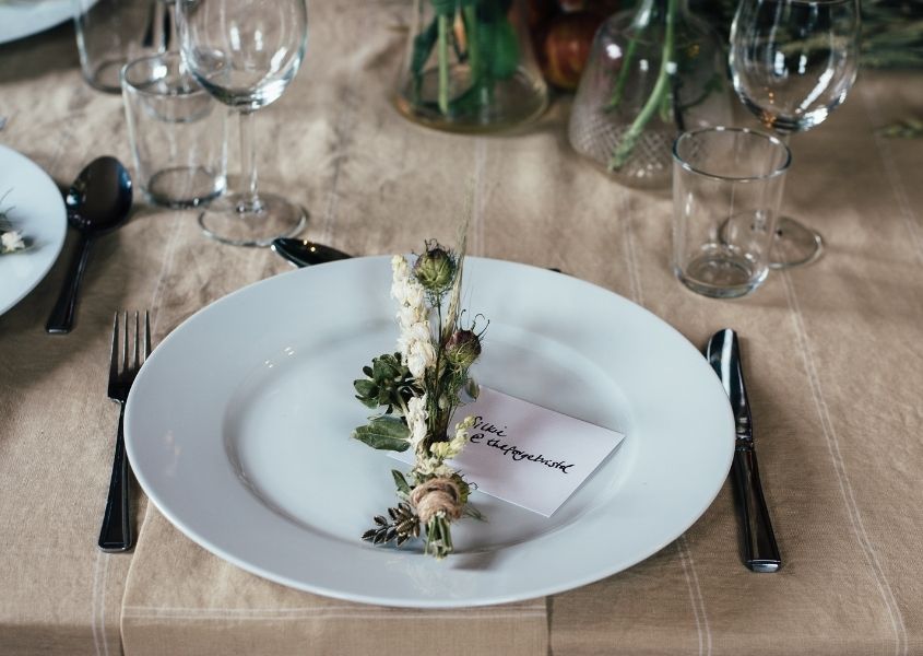 White plate on wood dining table with runner and small posy decoration on plate
