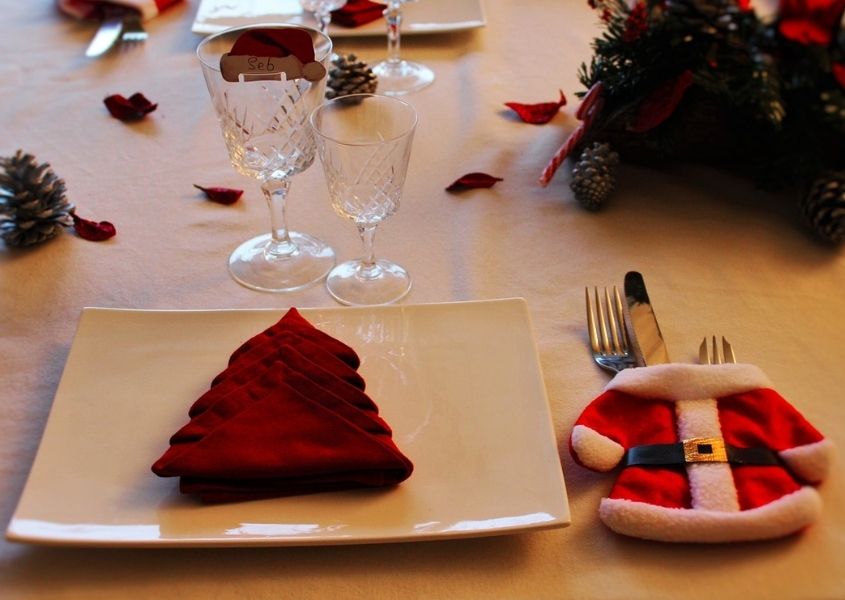 Close up of dinner table with red Christmas tree shaped napkin and Father Christmas cutlery pocket