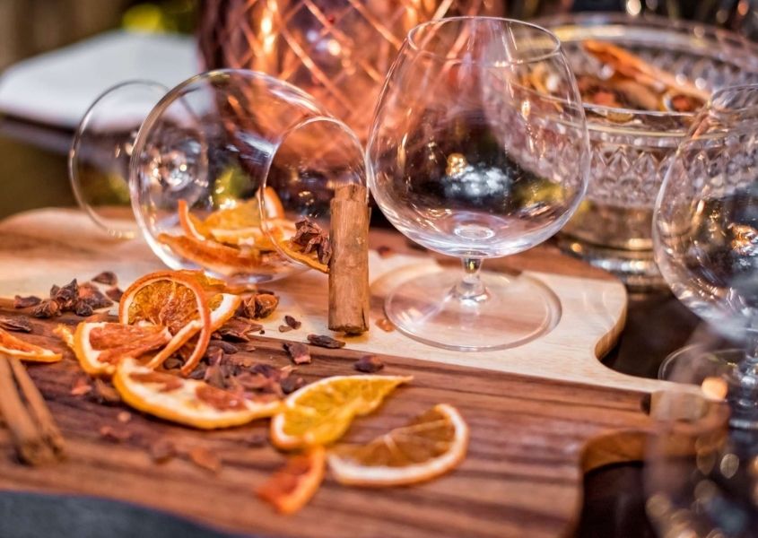 Dried orange slices and cinnamon sticks on wooden dining table with brandy glasses 