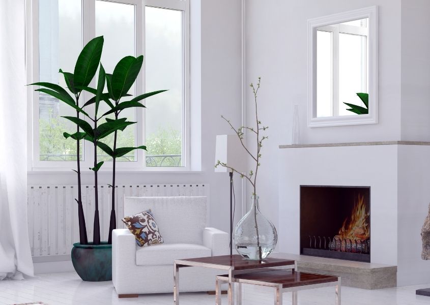 White living room with white armchair, mirror of fireplace and large green plant