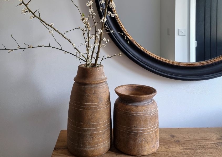 Terracotta vases on a rustic wooden sideboard with a black round mirror