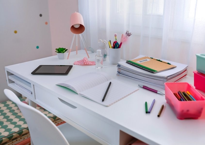 white desk with note pad, pens and pink desk lamp