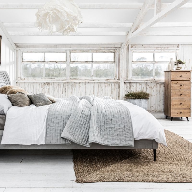 grey fabric bed with rustic tall chest of drawers