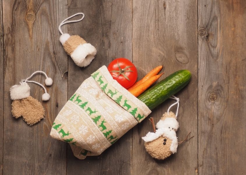 Cucumber, carrot and tomato in small sack on rustic wooden table with fabric Christmas decorations