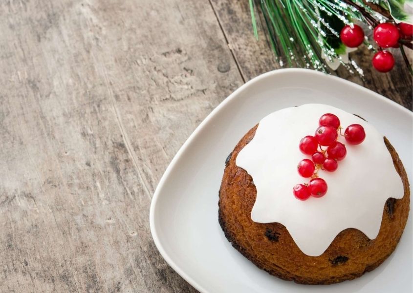 Vegan Christmas pudding with white icing on white plate and close up of pale wooden table
