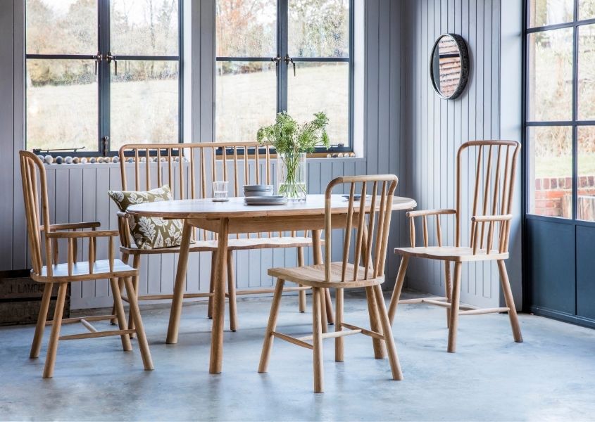 Pale wood dining table with matching spindle chairs in bright dining room with dark blue doors