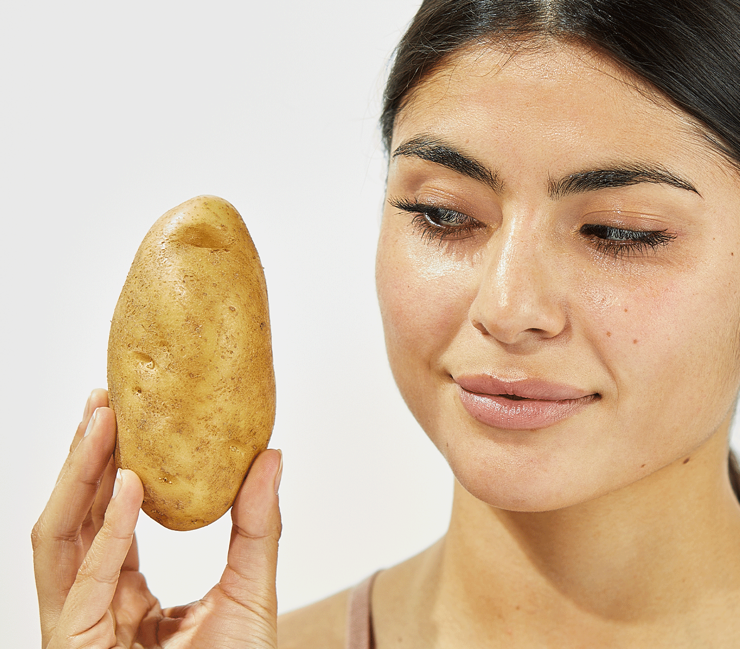 GIF image of a girl holding a potato up to her head and looking at it, and then the potato peel is replaced with Beekman 1802's Potato peel bottle and model has surprised look on her face.