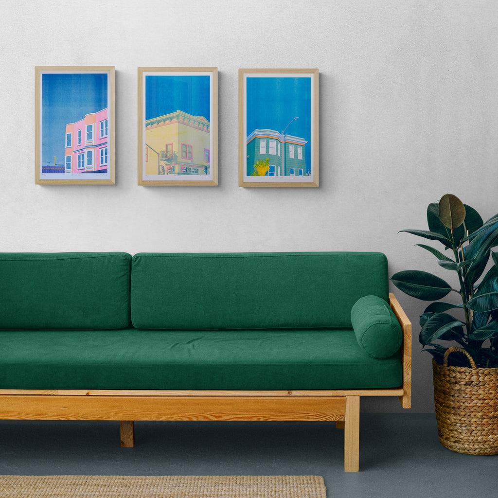 A green couch and a potted plant with framed prints of Hi-Bred risograph prints above the couch, creating a gallery wall