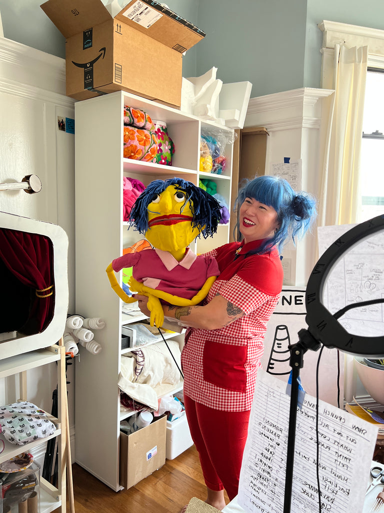 Risa holding a puppet of mini Risa in her studio