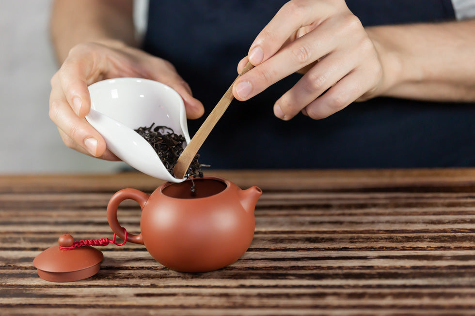 adding tea to teapot with wood utensil