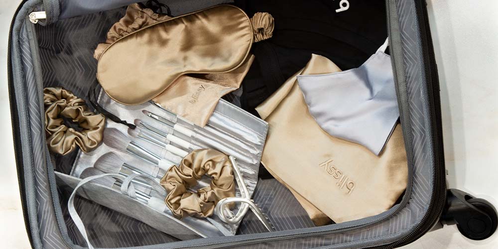 Travel luggage top view with Blissy silk sleep essentials in taupe and silver makeup brush