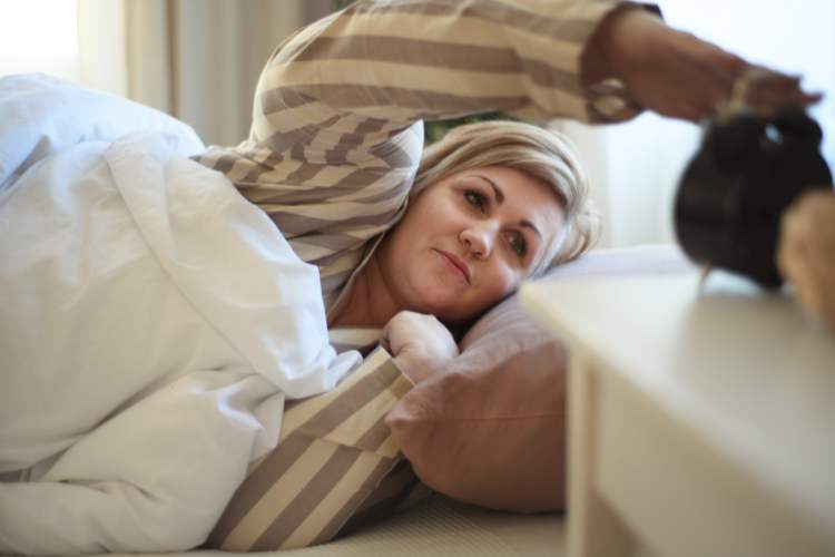 woman setting alarm from bed