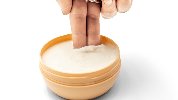 A person uses their fingers to get shea butter out of a pot