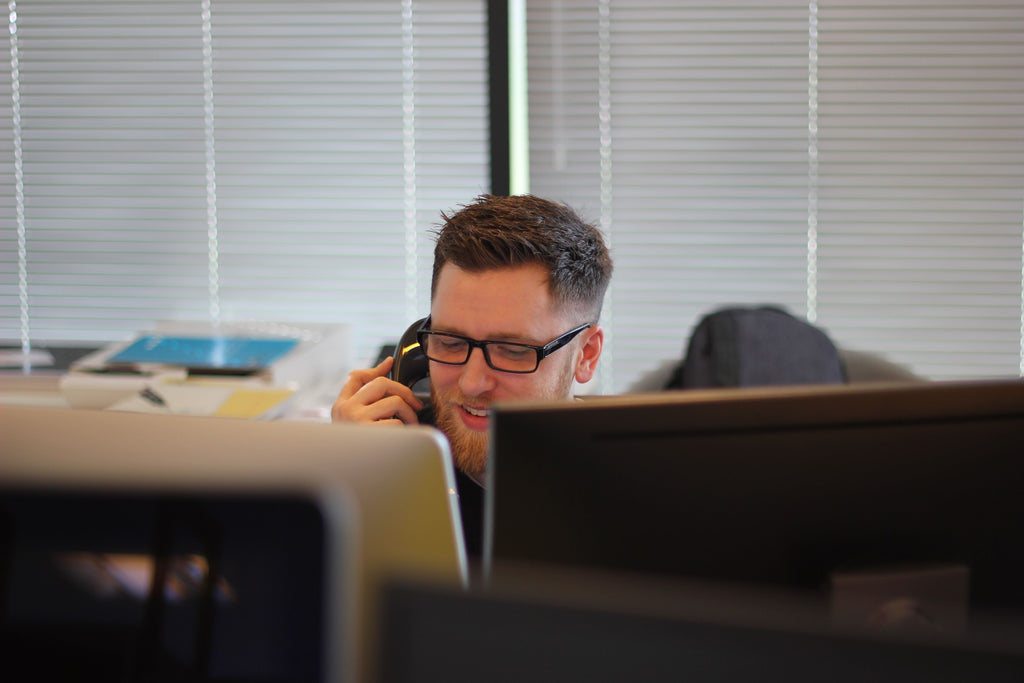 Man working in front of the computer while talking on the telephone.