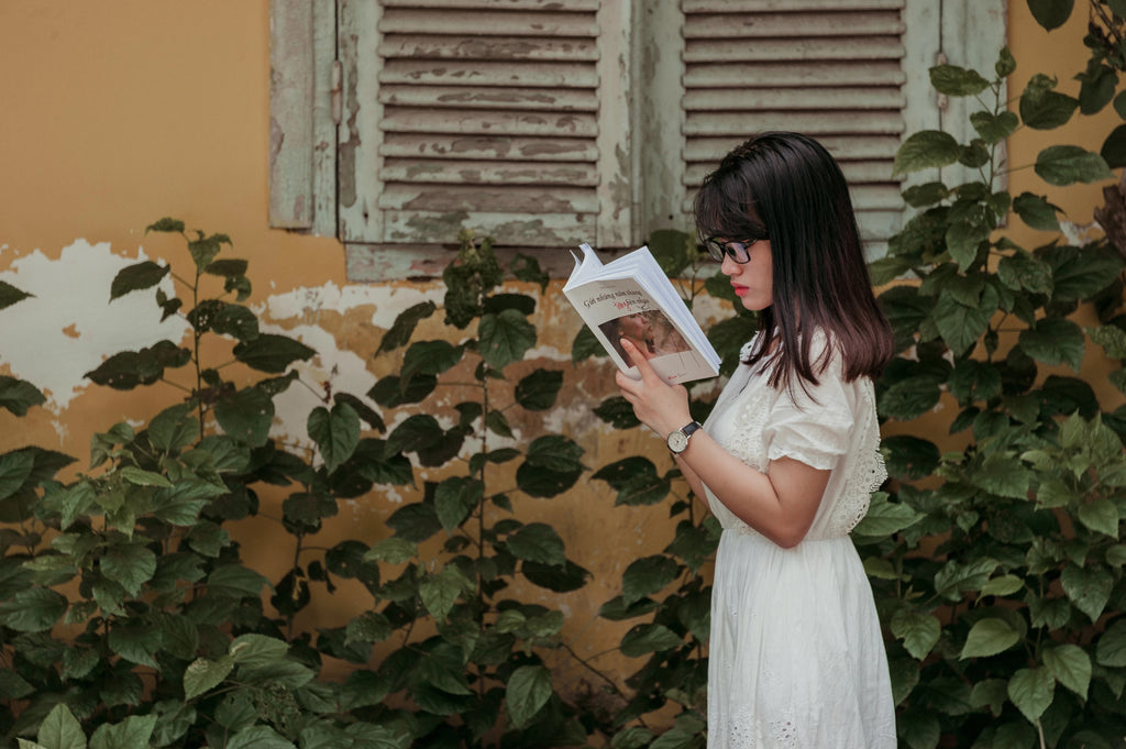 A girl reading while walking in the garden.
