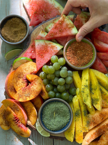 A fruit platter sprinkled with Well Seasoned Table spices and a hand reaching for a watermelon slice.
