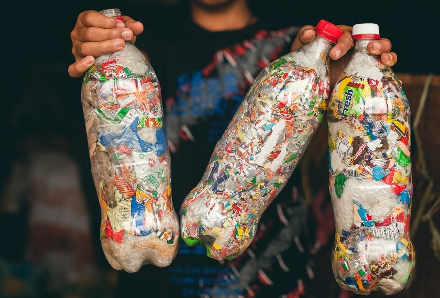 Person holding three ecobricks - plastic bottles stuffed with single-use plastics