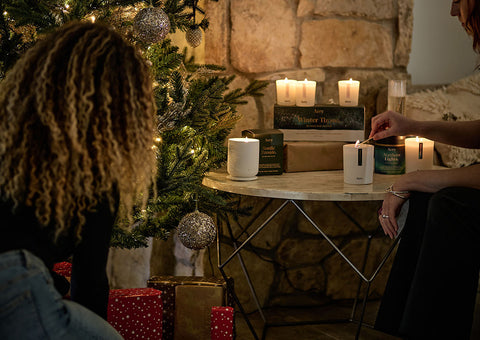 two people in front of a christmas tree with candles and presents