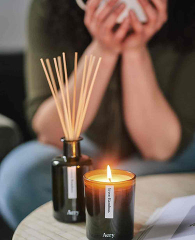 person drinking a hot drink with magazine, lit candle and a diffuser