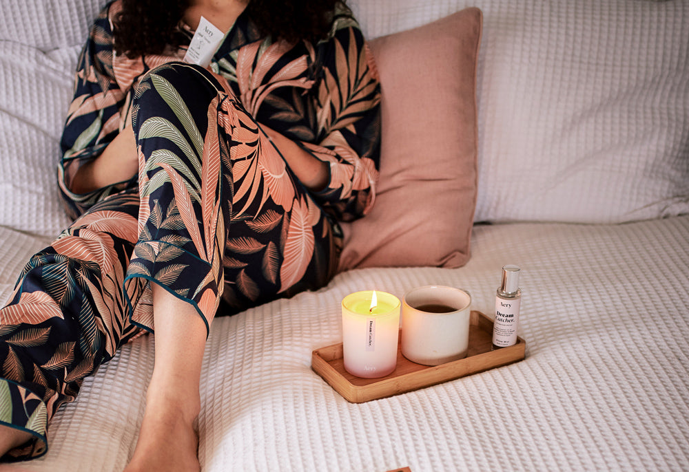 person laying on bed with cup of tea and lavender candle
