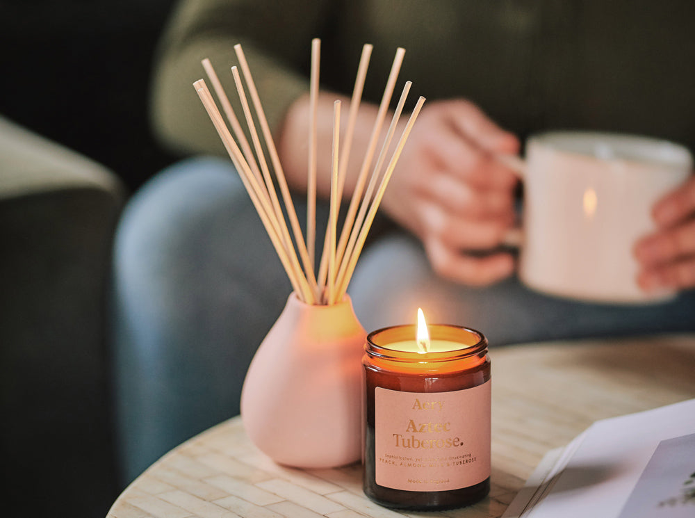 pink peach scented candle and matching reed diffuser displayed on coffee table with person in the background