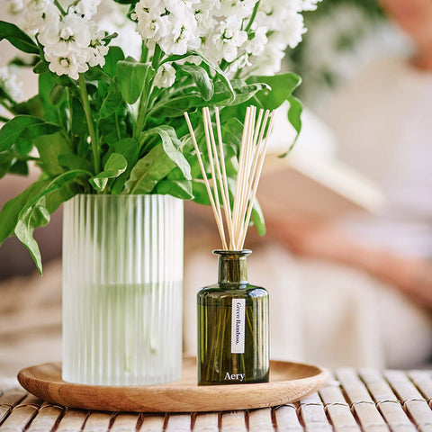 Green Bamboo reed diffuser by Aery placed next to vase of flowers