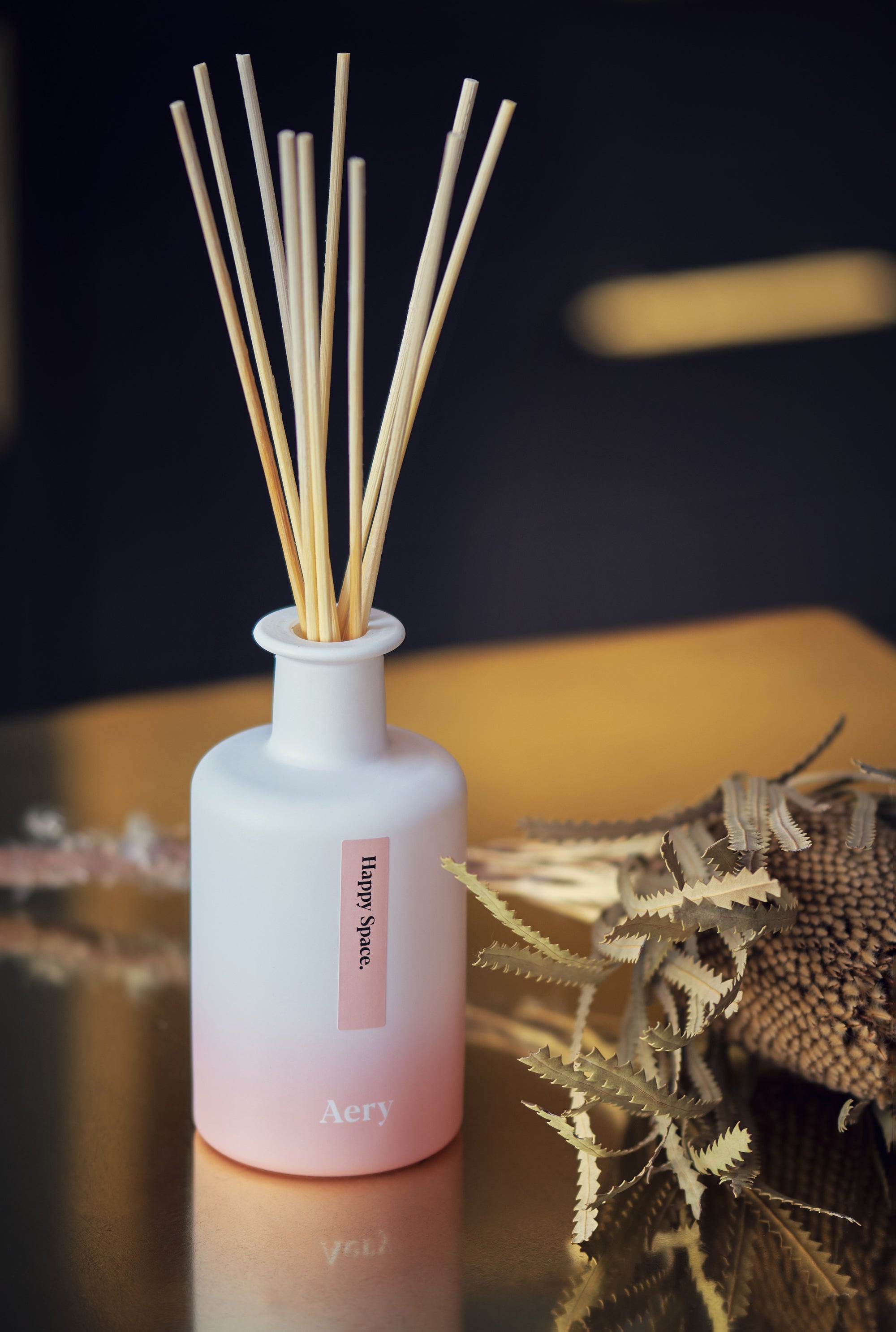 happy space reed diffuser by aery living displayed on a brass counter top next to decorative dried flower