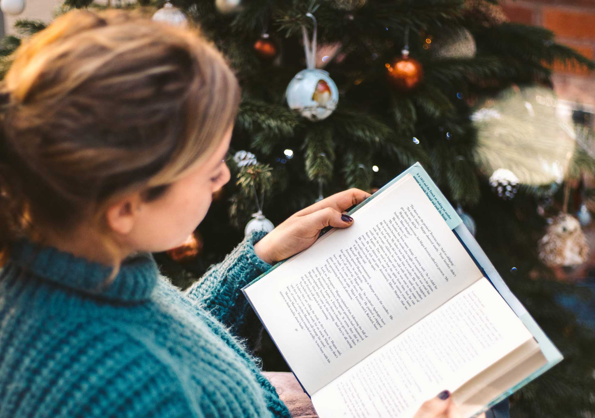 woman sat next to christmas tree reading a book
