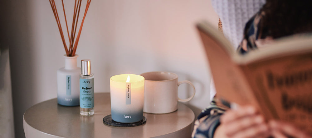 person reading in bed with scented candle and diffuser on bedside table