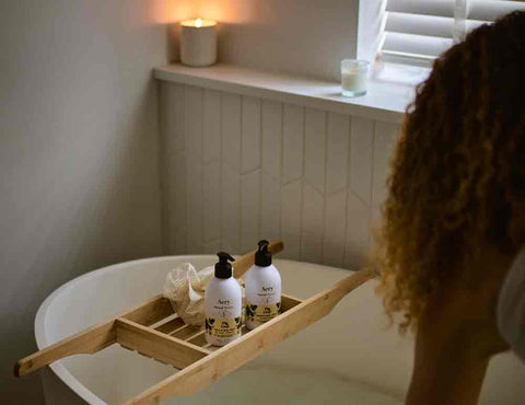 person running a bath with body wash and lotion displayed on bath caddy