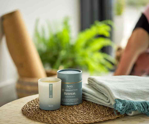 aery yoga candle displayed next to product packaging with person doing yoga pose in the back gound