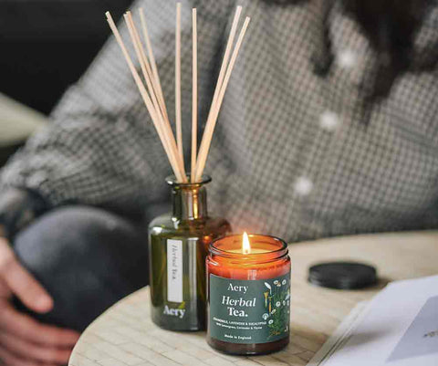 herbal tea jar candle and matching diffuser on coffee table with person reading magazine in the back ground