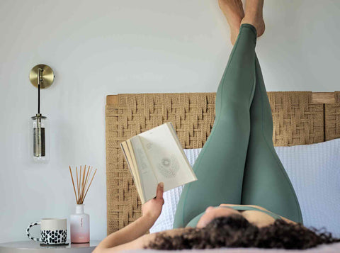 person relaxing and reading in bed with their legs raised against the headboard