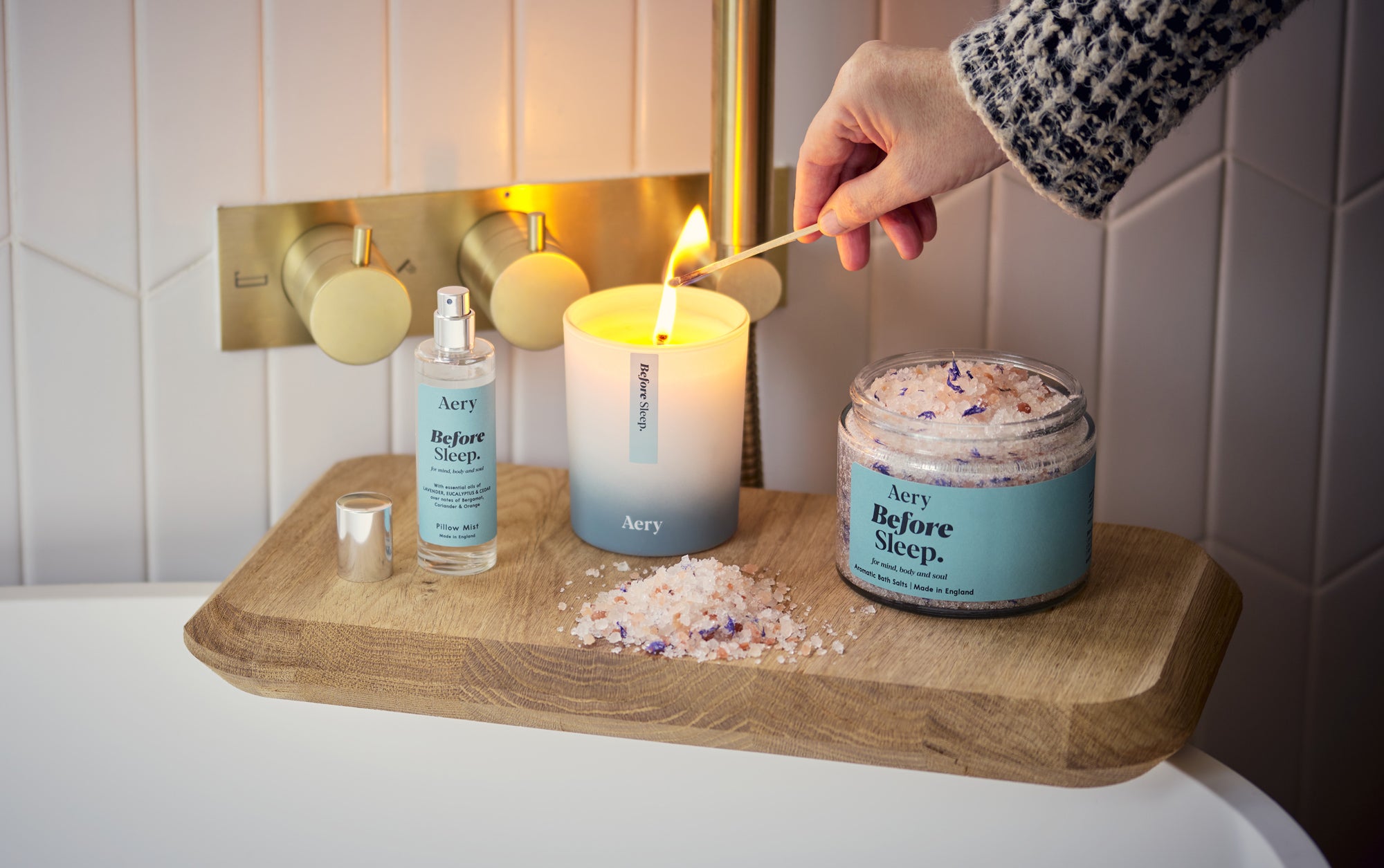 aery living bath salts candle and pillow mist with person lighting candle in a bathroom setting