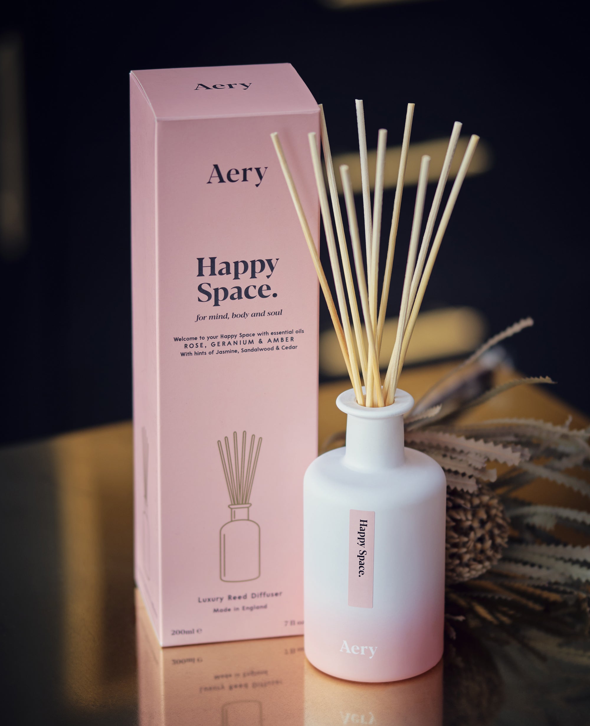 aery living pink happy space reed diffuser next to product packaging displayed on a brass counter top