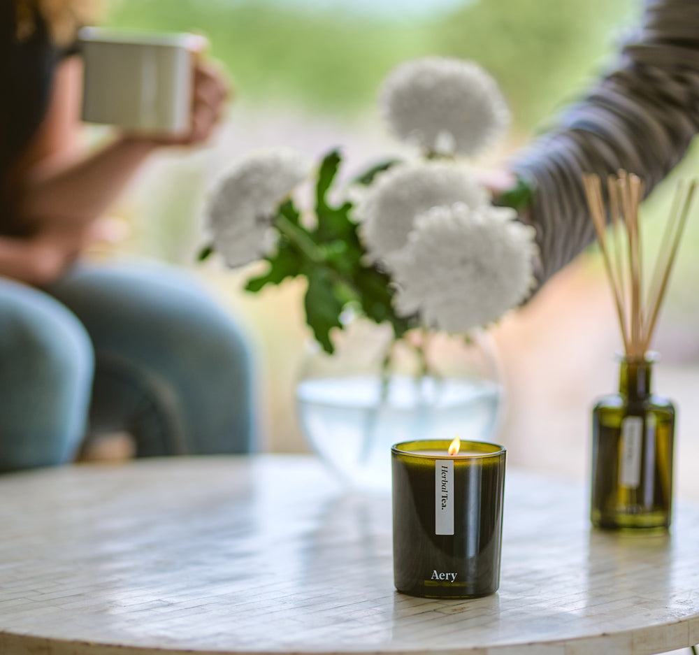 herbal tea scented candle and diffuser displayed on coffee table in front of a vase of flowers