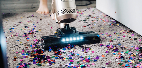 someone using a vacuum to clean confetti off carpet