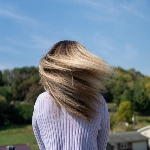a woman wearing a purple sweater shakes her blonde hair outside on a sunny day