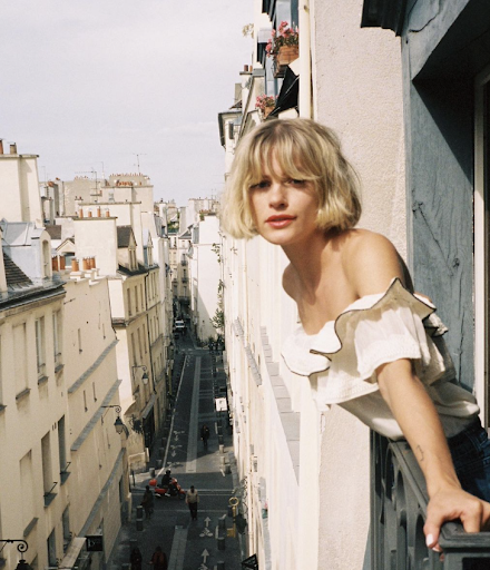Girl with blonde French bob as she leans out of window in Paris.
