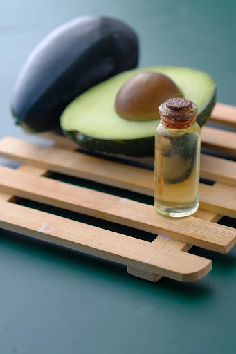 Image of avocado and a bottle of oil on a wooden table.